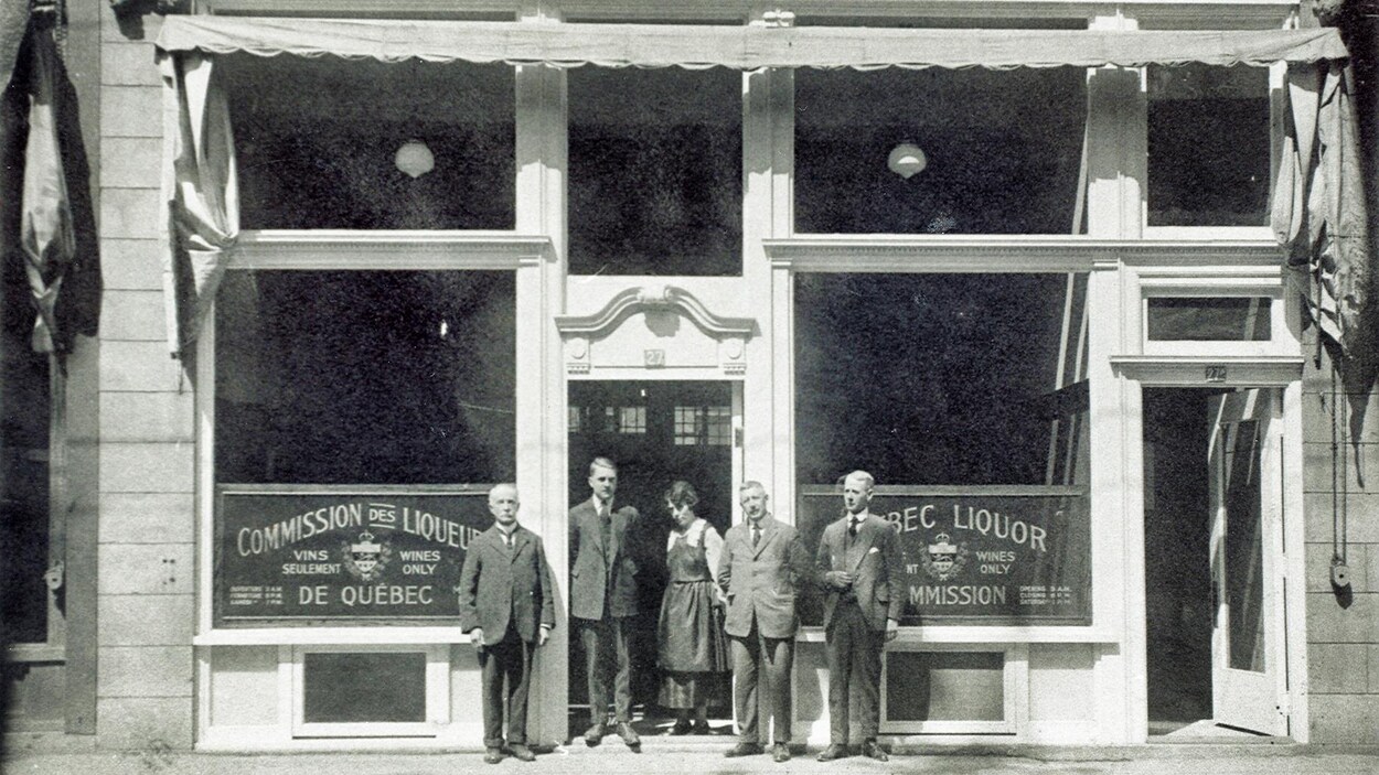 Des gens prennent la pose devant l'un des premiers magasins de la Commission des liqueurs de Québec, durant les années 1920. A l'époque, les produits sont bien cachés derrière des grilles, et ne s'affichent pas en vitrine. Des gens prennent la pose devant l'un des premiers magasins de la Commission des liqueurs de Québec, durant les années 1920. A l'époque, les produits sont bien cachés derrière des grilles, et ne s'affichent pas en vitrine.
