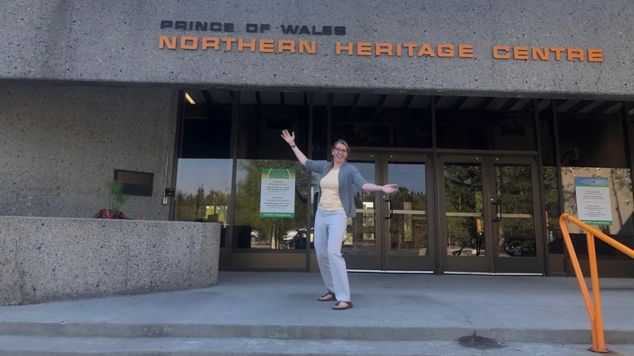 La directrice Sara Carr-Locke est debout en souriant devant la porte d'entrée du Centre du patrimoine septentrional