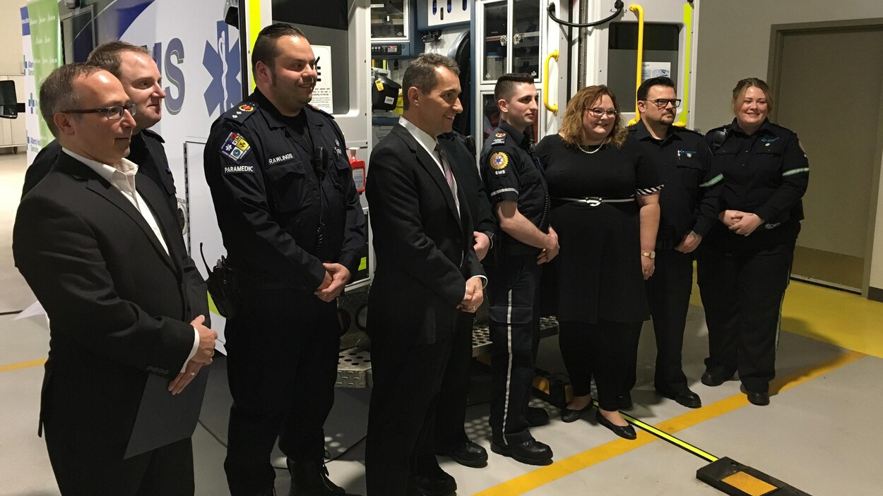 La ministre de la Santé, Sarah Hoffman, entourée d'ambulanciers devant une ambulance.