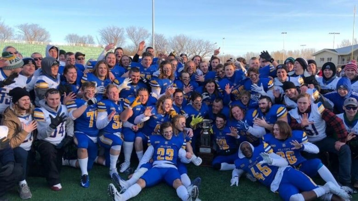 L'équipe des Hilltops, regroupée sur le terrain pour une photo avec la coupe. Les joueurs contents montrent les cinq doigts de la main pour signifier qu'ils détiennent le titre de champion depuis 5 ans.