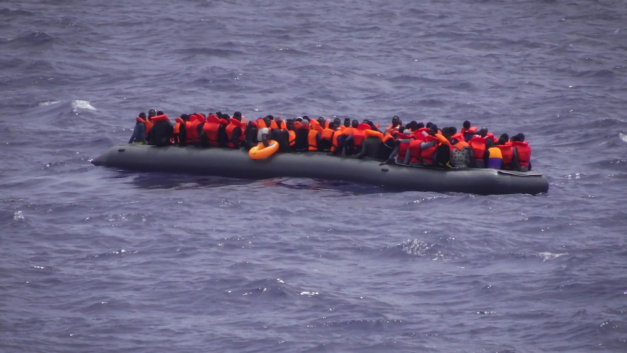 Une embarcation remplie de migrants flotte sur la mer. Une embarcation remplie de migrants flotte sur la mer.