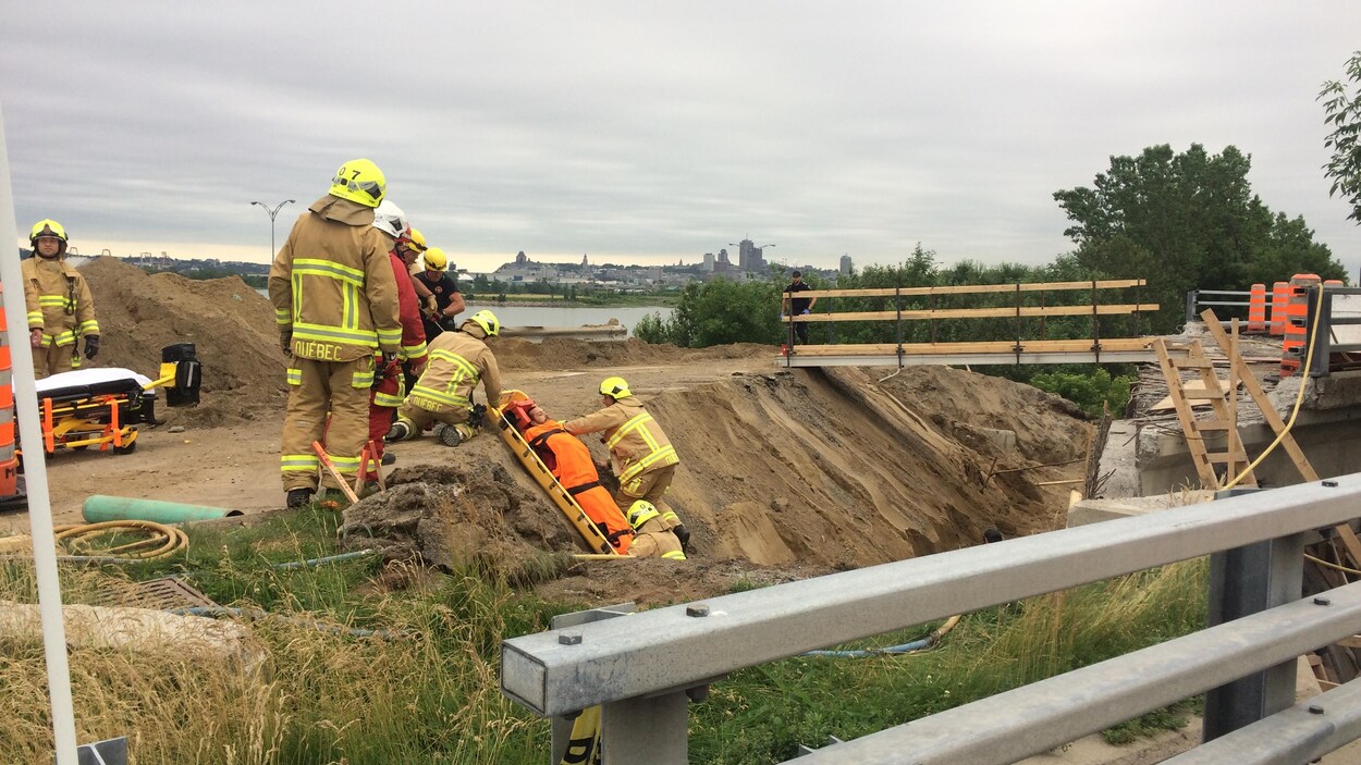 Des pompiers aident un homme sur une civière à sortir d'une tranchée.