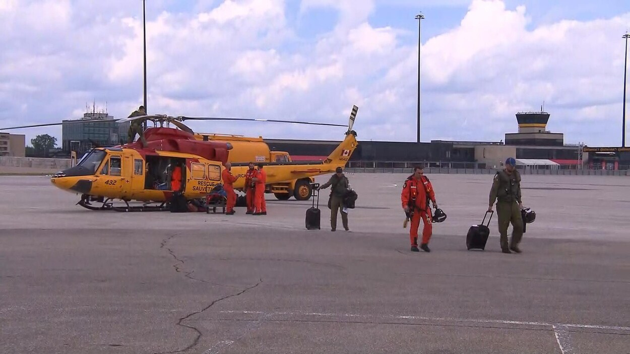 Des secouristes marchent sur un tarmac où se trouve un hélicoptère jaune.