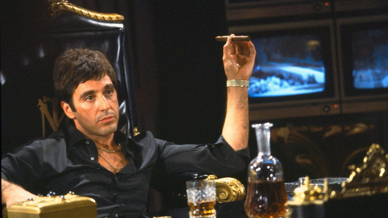 L'acteur Al Pacino assis dans un fauteuil, un cigare à la main, dans une scène du film « Scarface ».