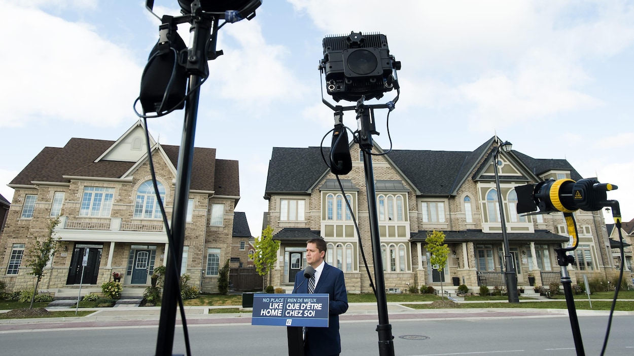 M. Scheer s'adresse aux médias devant des maisons en rangée.