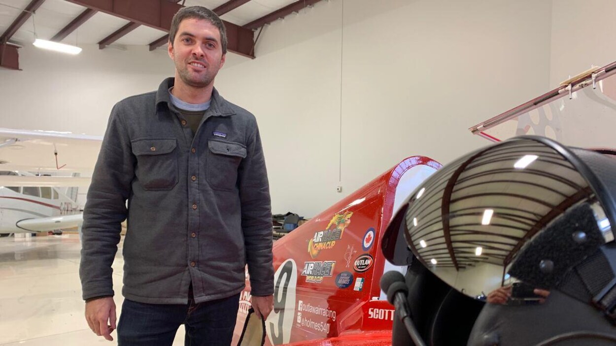 Scott Holmes dans un hangar de l'aéroport de Villeneuve. Il se tient à côté d'un prototype d'avion.