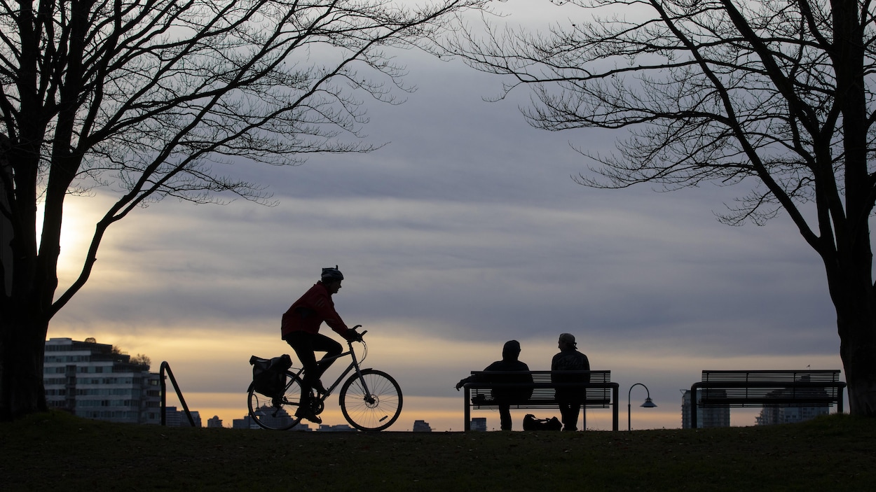 Un cycliste et des gens assis sur un banc dans un parc de Vancouver au coucher du soleil.