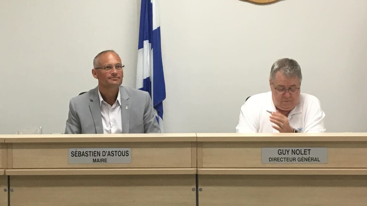 Sébastien D'Astous et le directeur général de la Ville, Guy Nolet, assis devant le public lors du conseil municipal.