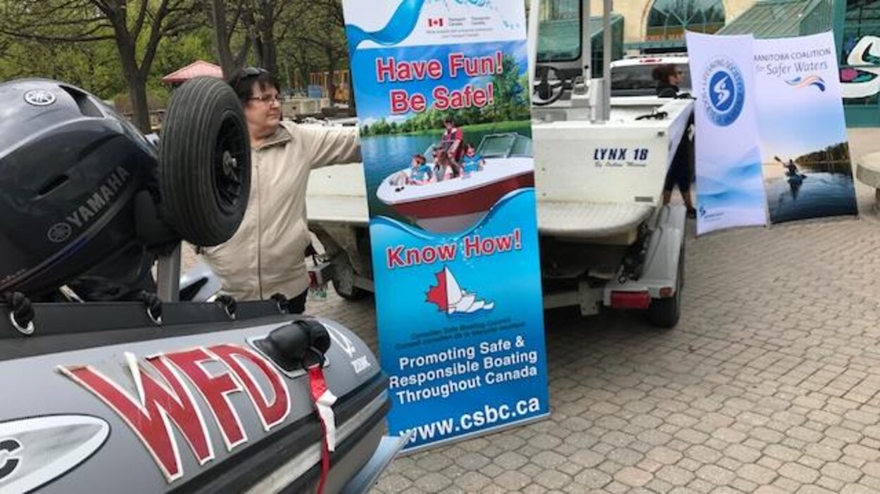 Une femme tient une affiche promouvant les règles de sécurité en bateau, entre deux embarcations de services de secours. Une femme tient une affiche promouvant les règles de sécurité en bateau, entre deux embarcations de services de secours.