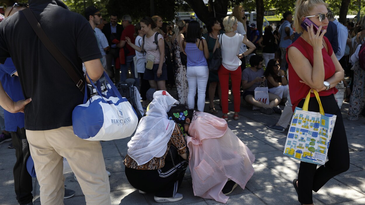Des femmes agenouillées s'enlacent sur une place publique, au milieu d'une foule.