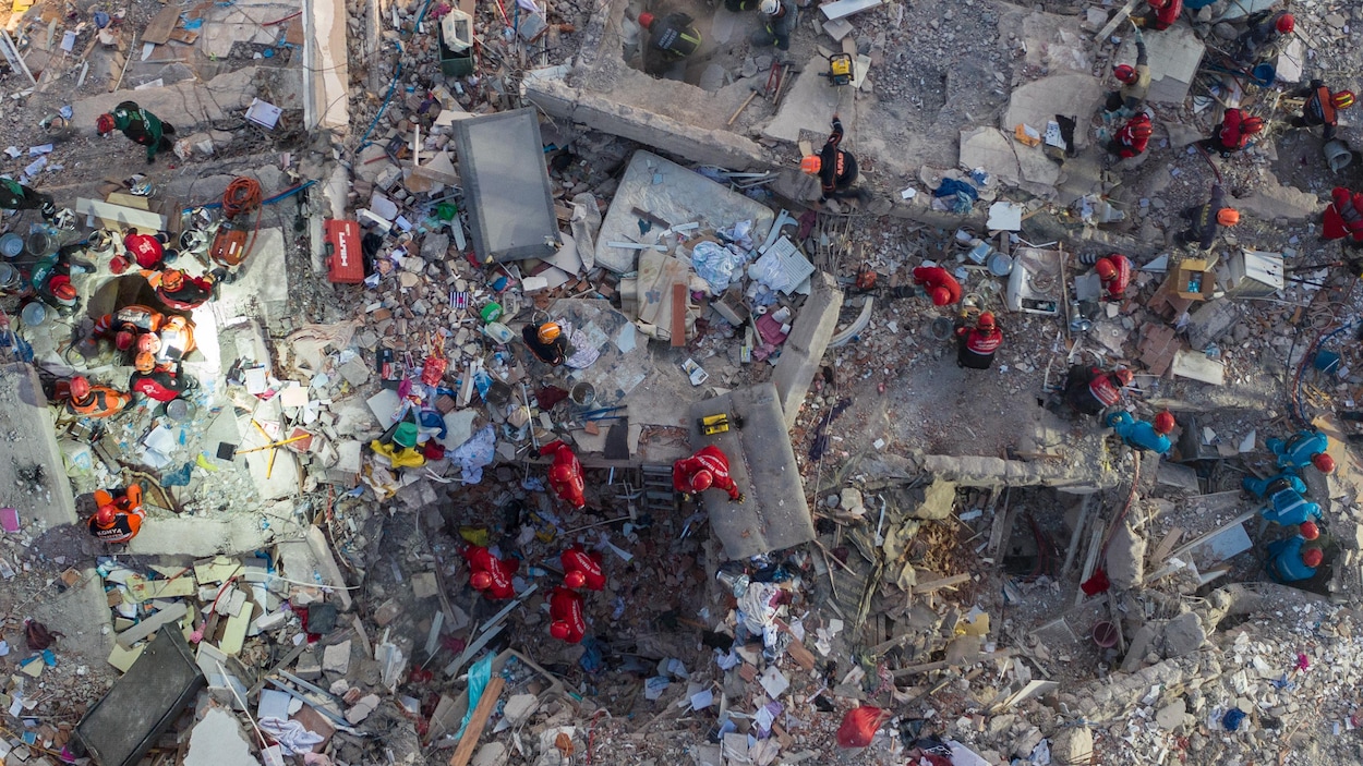 Vue du ciel d'un bâtiment détruit par le séisme. On y voit plusieurs secouristes tenter de retrouver des survivants.