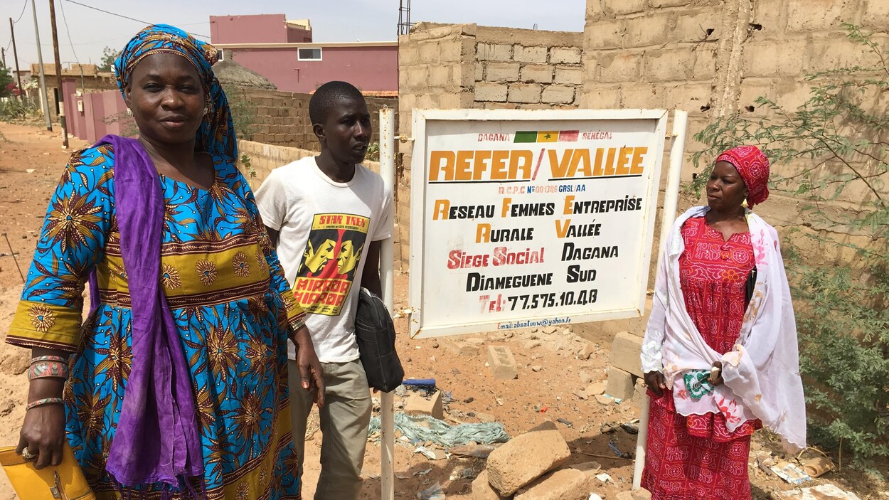 Lors d'une journée ensoleillée, deux femmes et un homme posent devant une pancarte sur laquelle on peut lire « Réseau femmes entreprise rurale vallée ». 