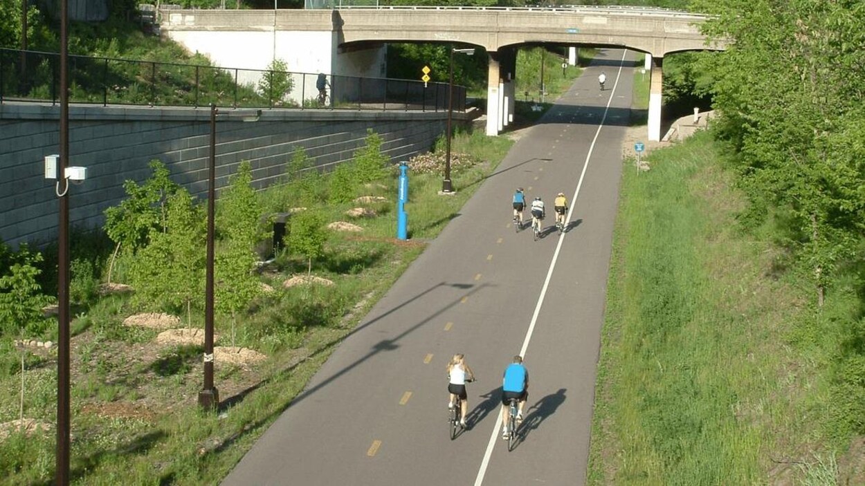 Un large sentier pour vélo entouré de végétations, sur lequel circulent quelques personnes. Un large sentier pour vélo entouré de végétations, sur lequel circulent quelques personnes.