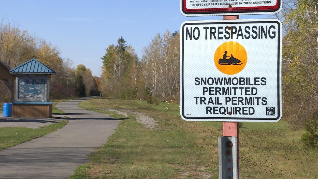 Un panneau de métal sur lequel on peut lire « No Trespassing » à l'entrée d'un sentier boisé.