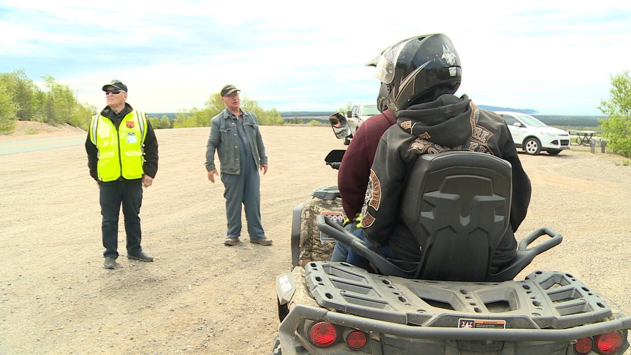 Deux personnes sur un quad sont arrêtées et parlent avec deux autres hommes.