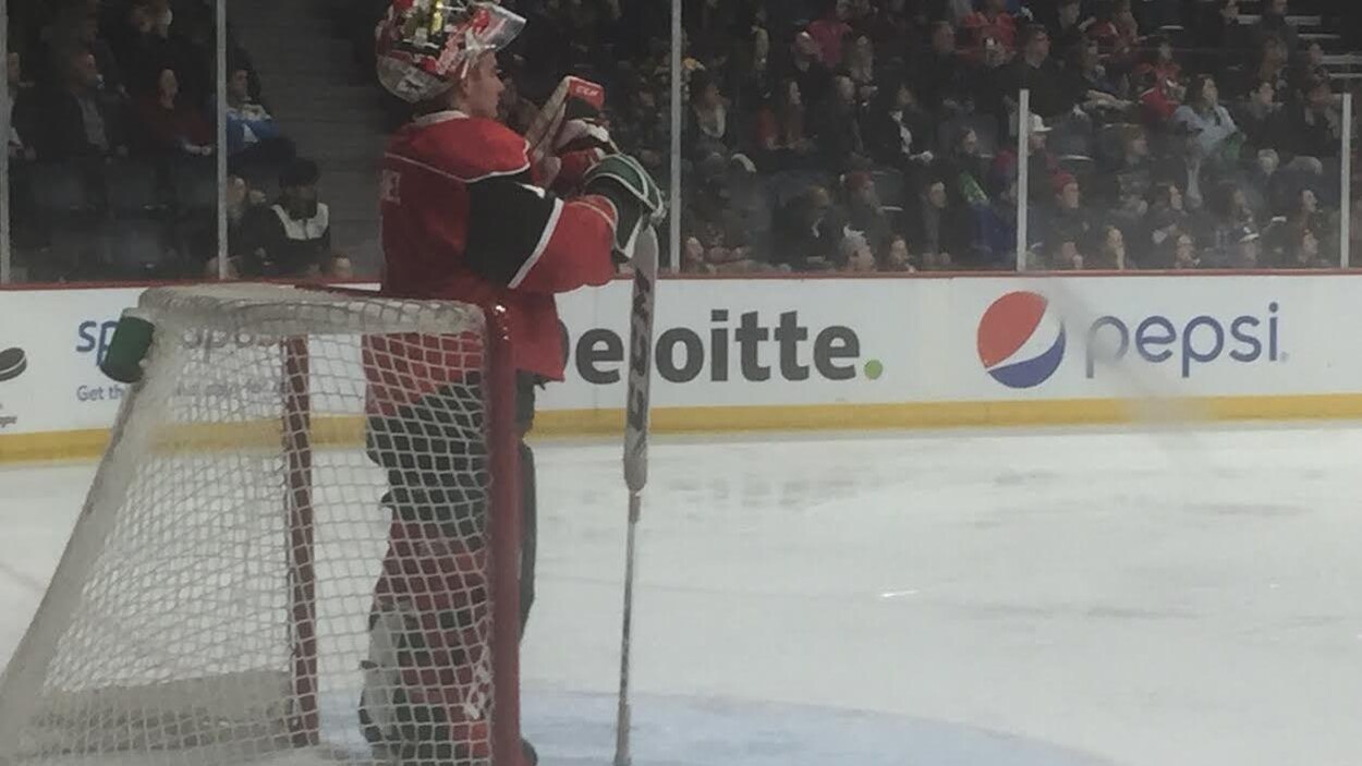 Un gardien de but au hockey s'appuie sur son bâton devant son filet