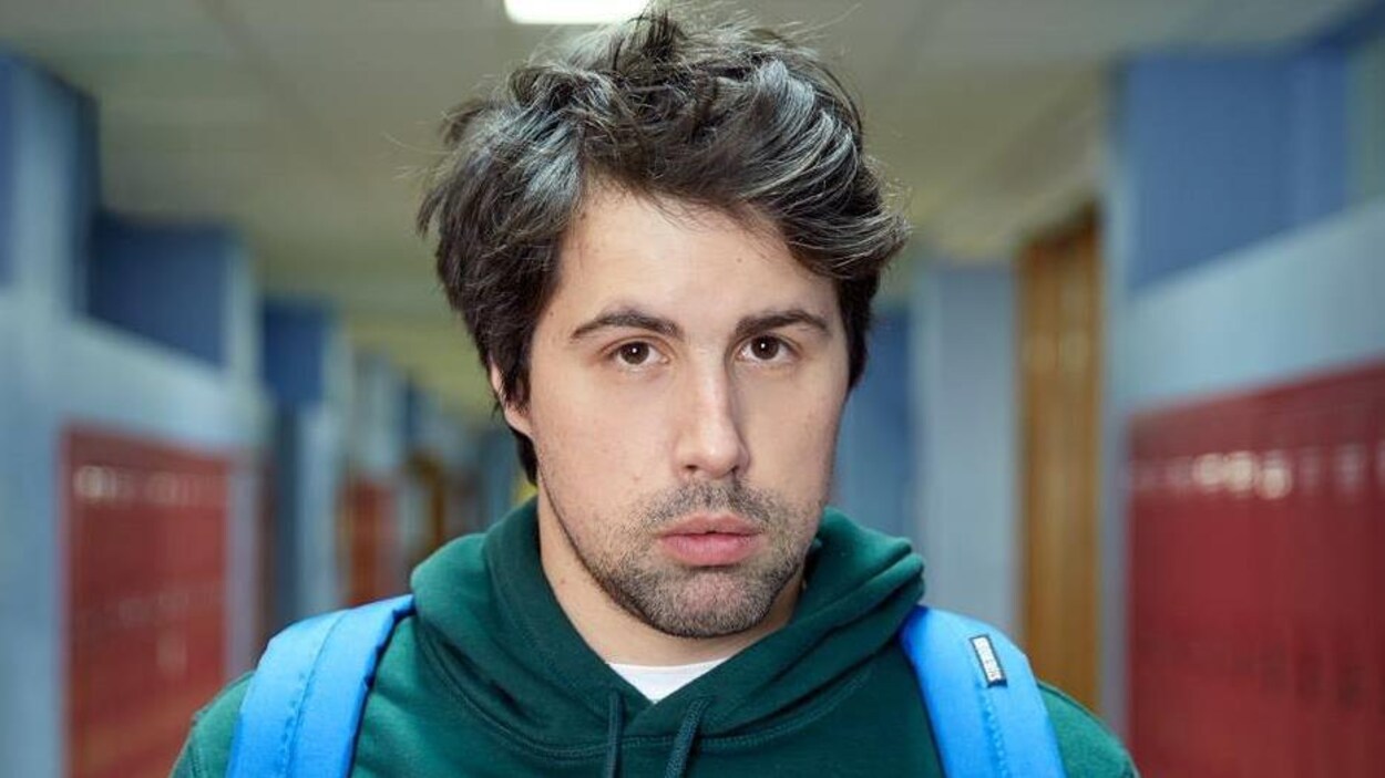 Philippe-Audrey-Larrue-St-Jacques est dans un couloir d'école, et porte un sac à dos.
