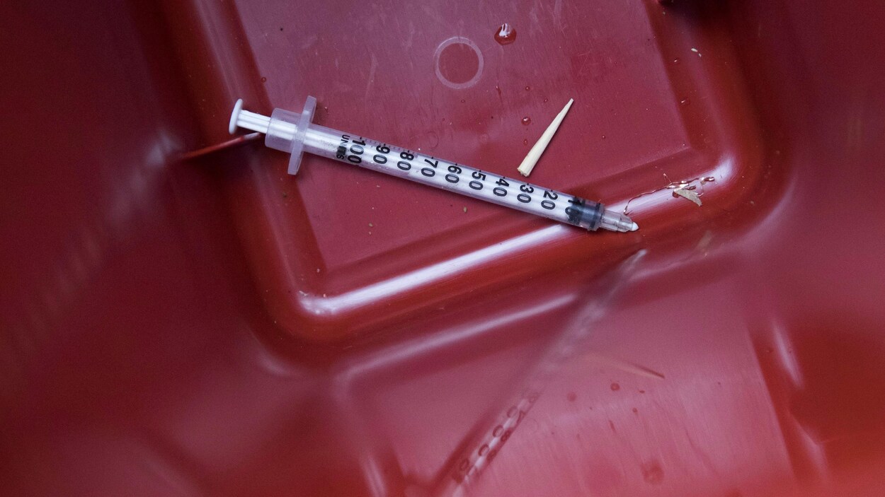 Gros plan sur une seringue cassée avec reflet sur un bac rouge.