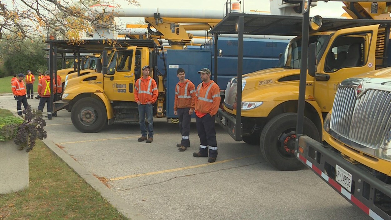Des travailleurs devant des camions lourds de la Ville de Toronto.