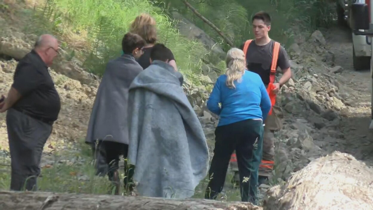 Deux jeunes recouvert de couvertures, trois adultes et un pompier dans la nature.
