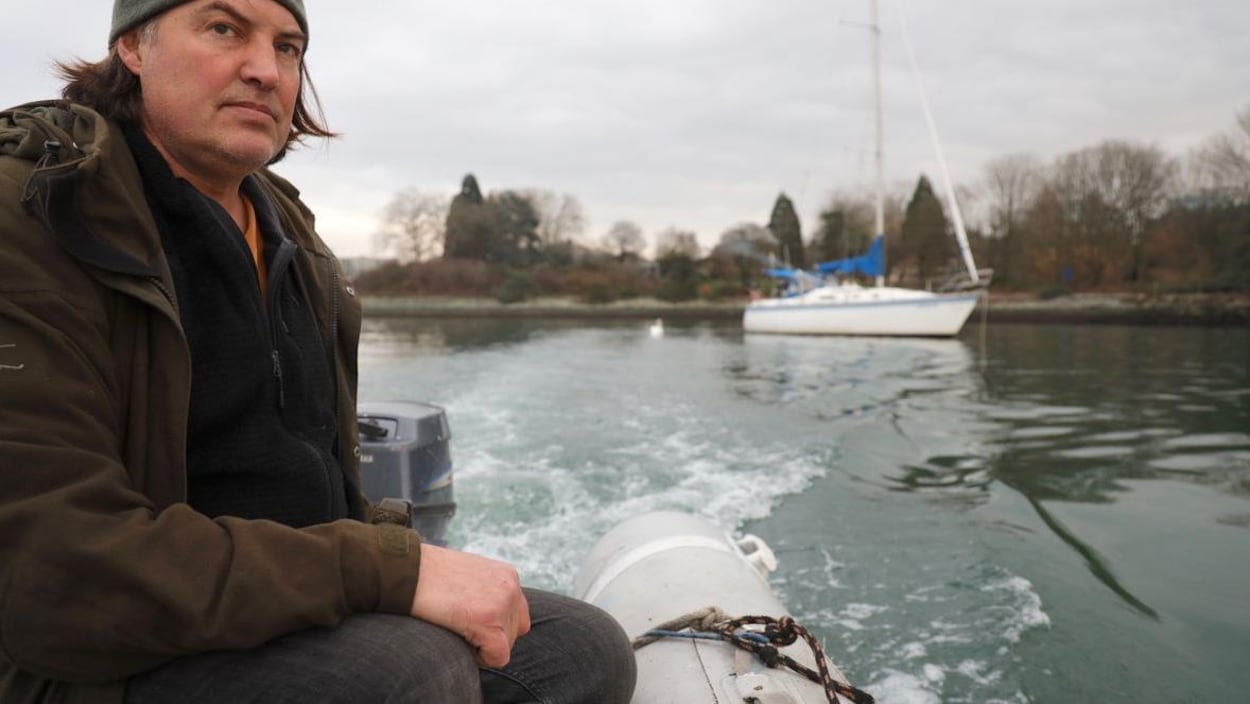 Un homme porte une tuque et un manteau. Il regarde l'horizon en conduisant son bateau.