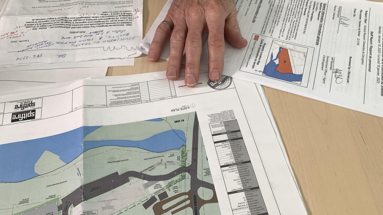 Une main d'homme est posée sur des plans et des documents étalés sur une table de cuisine.