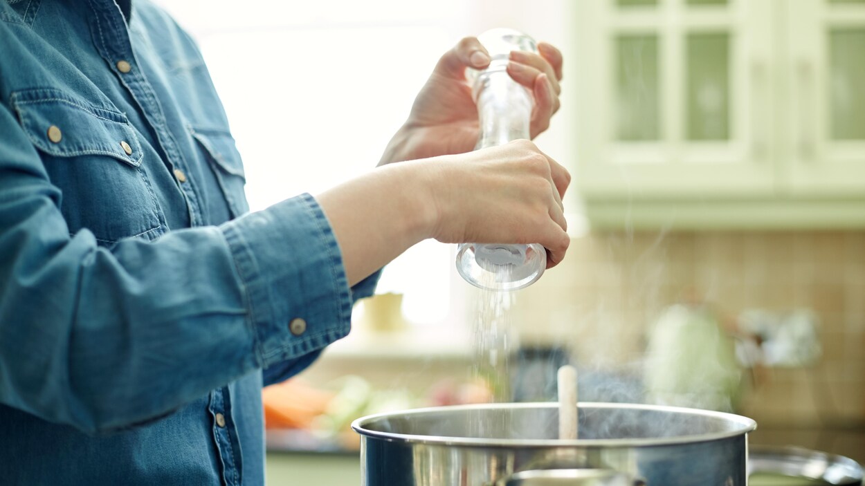 Une personne met du sel dans sa casserole sur le feu.