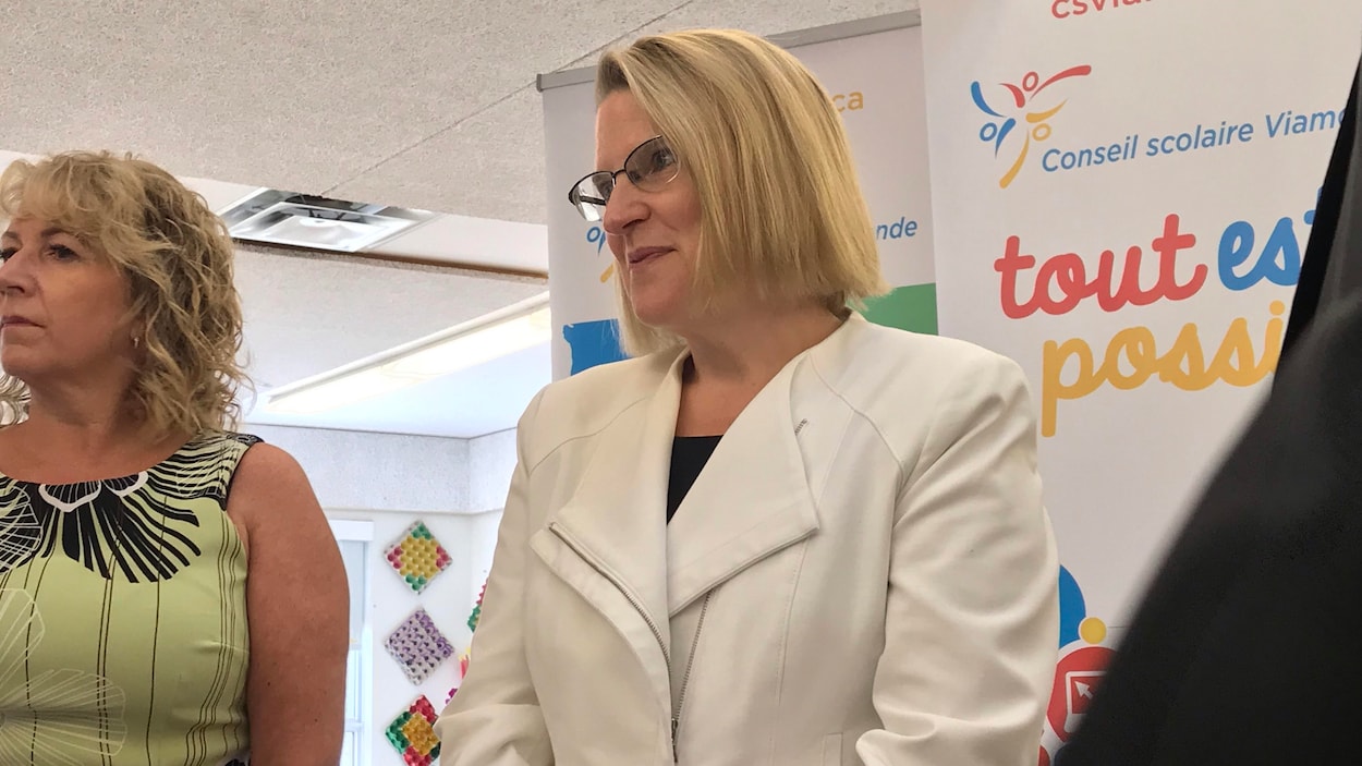 Une femme en veston blanc aux côtés d'une femme en robe verte, devant une bannière aux couleurs du Conseil scolaire Viamonde