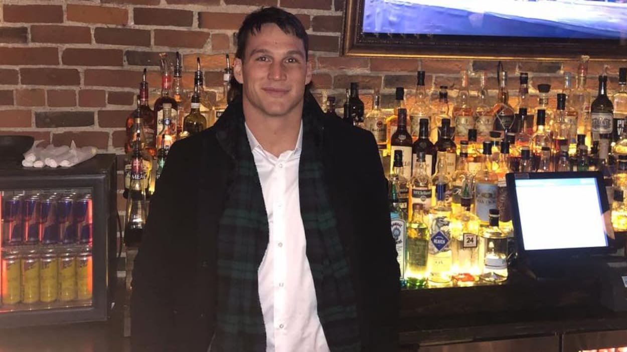 Un homme devant un bar rempli de bouteilles d'alcool.
