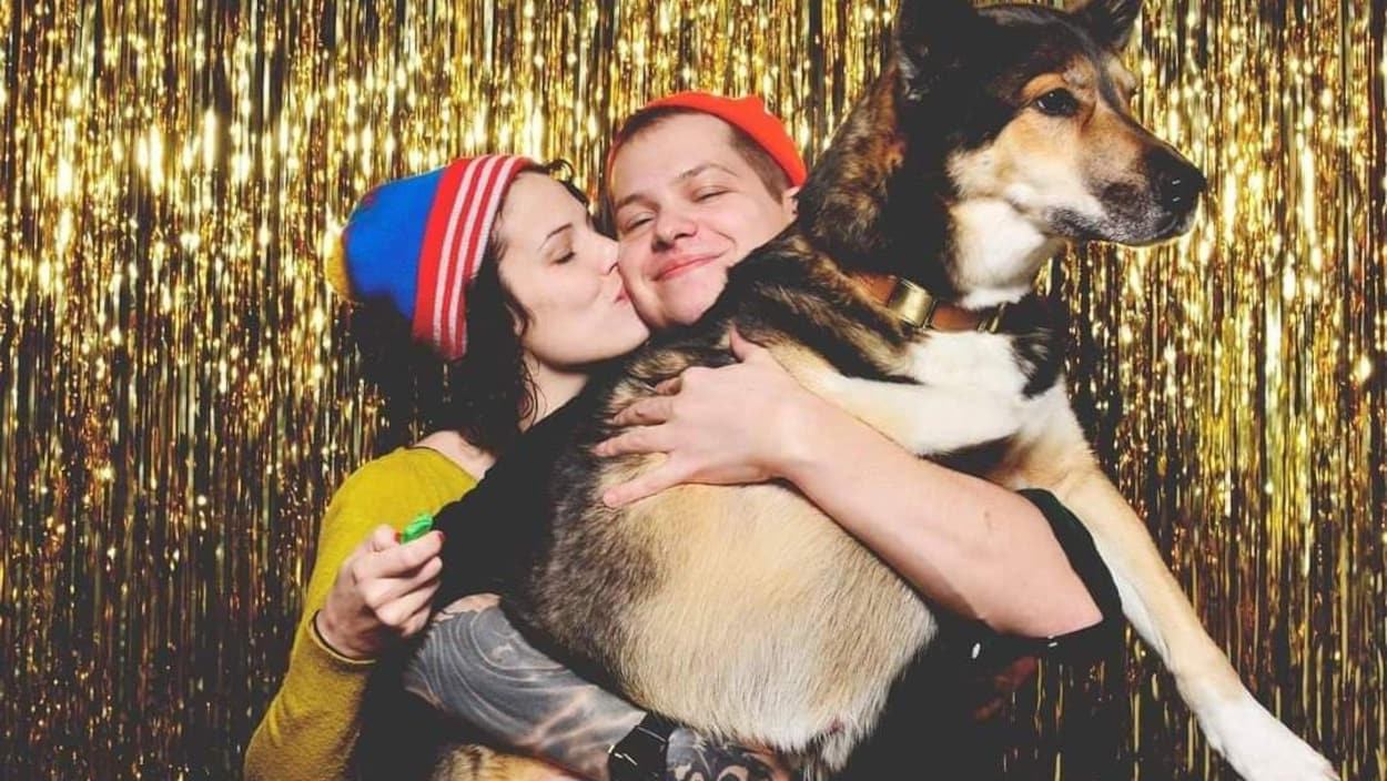 Alexandrine donne un bisou sur la joue à Simon qui tient le chien dans ses bras.