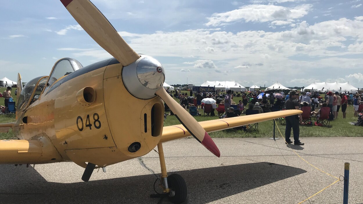 Le devant d'un avion à hélice vu de près avec, en arrière-plan, une foule assemblée sur l'herbe.