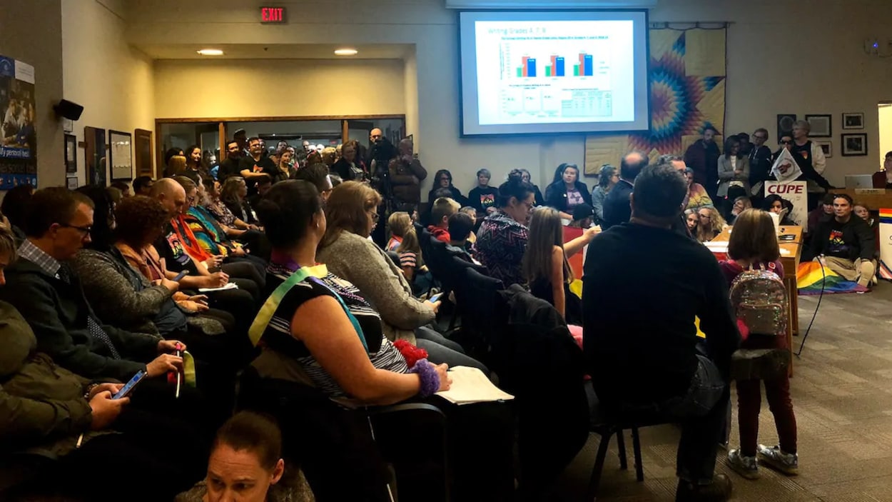 Des gens assis dans une salle regardent un graphique montrant les résultats du vote projeté sur un écran.
