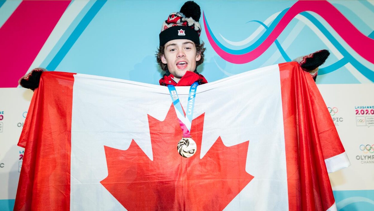 L'athlète porte sa médaille d'or et tient un drapeau canadien devant son torse.