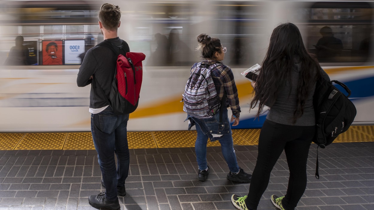 Trois passagers devant un train qui passent rapidement.