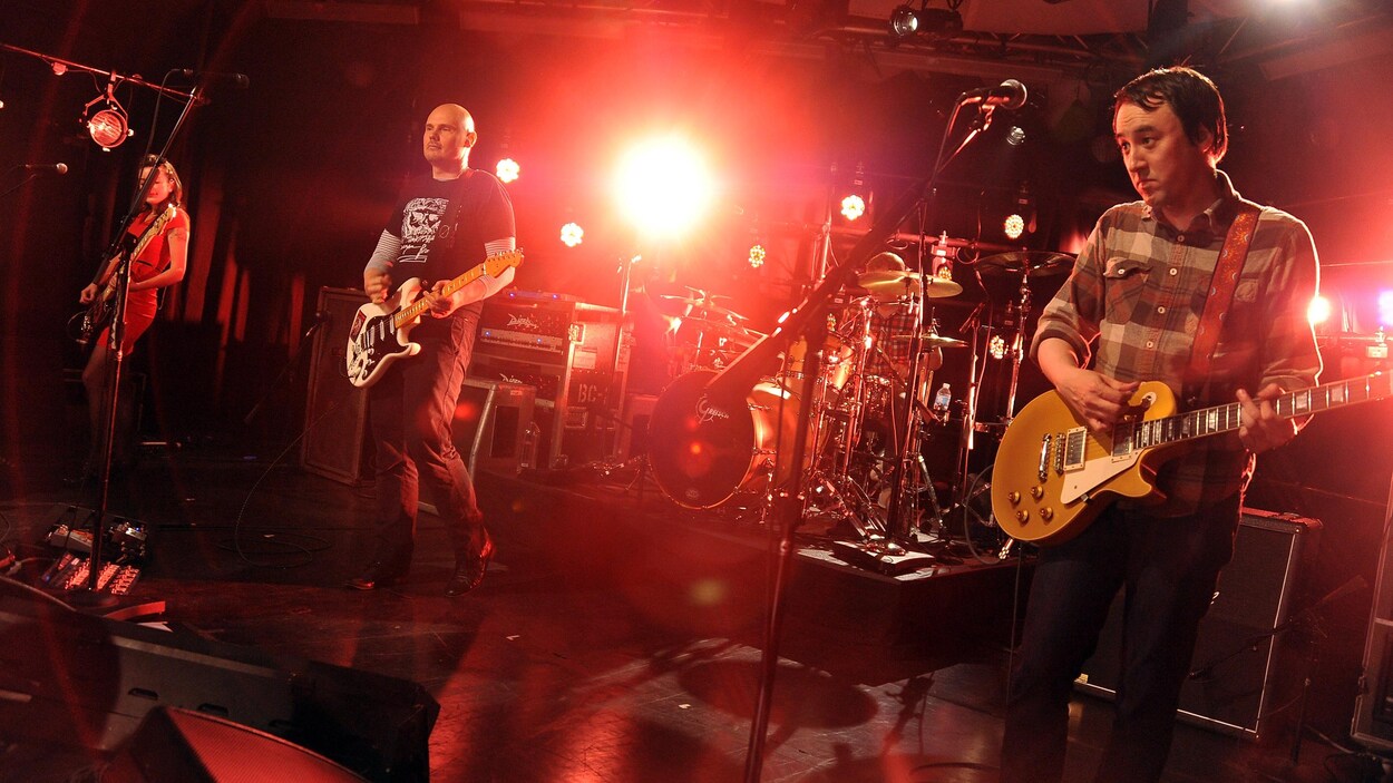 Le groupe Smashing Pumpkins sur une scène illuminée de rouge. Le groupe Smashing Pumpkins sur une scène illuminée de rouge.