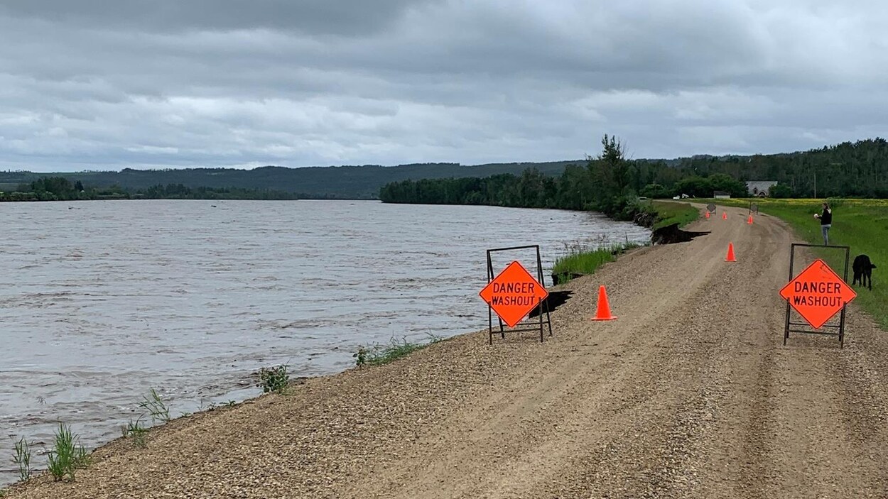 Une route le long de la rivière est jonchée par des cônes et des panneaux qui signalent « Attention : affaissement ».