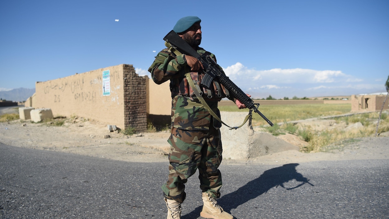 Un homme en treillis militaire tient un fusil, debout au milieu d'une route.