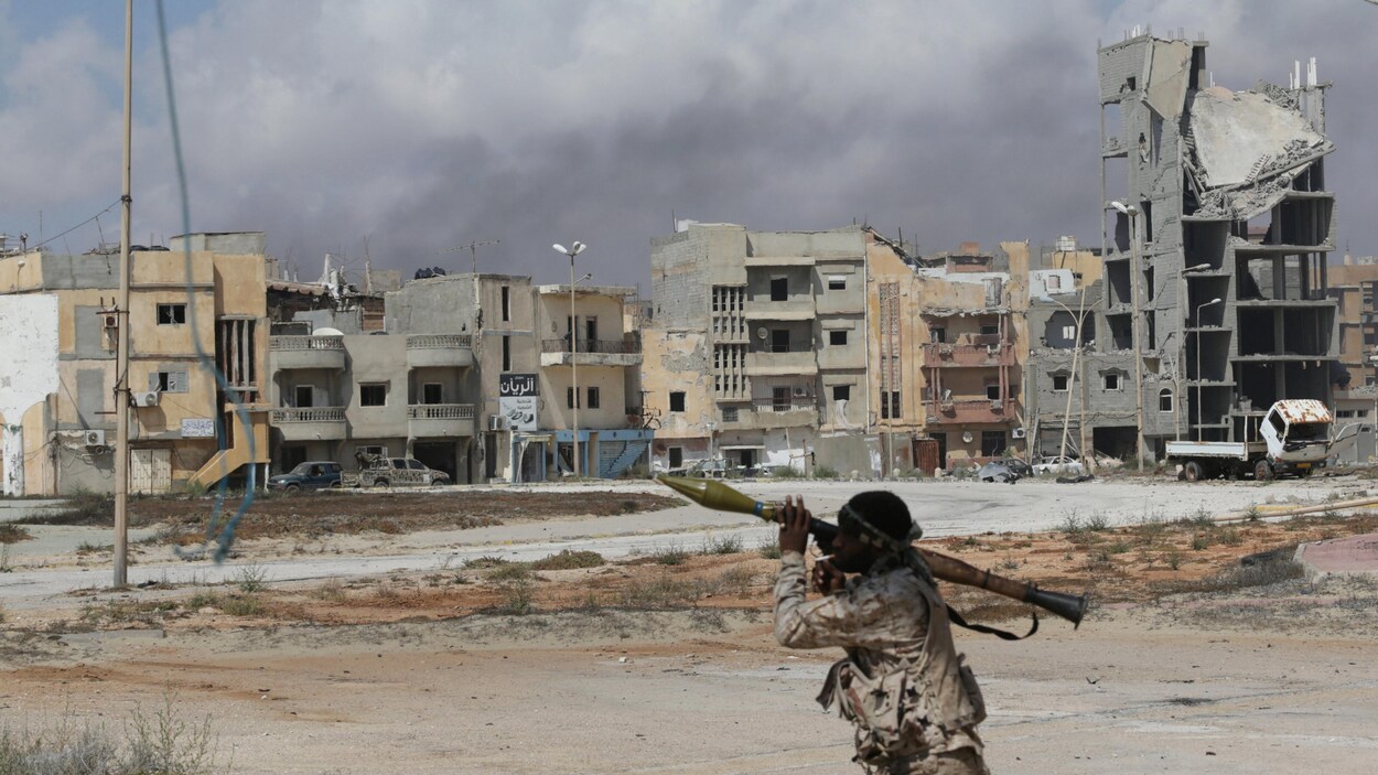 Un soldat de l'Armée nationale libyenne tient un lance-roquettes. On le voit devant un quartier largement démoli.