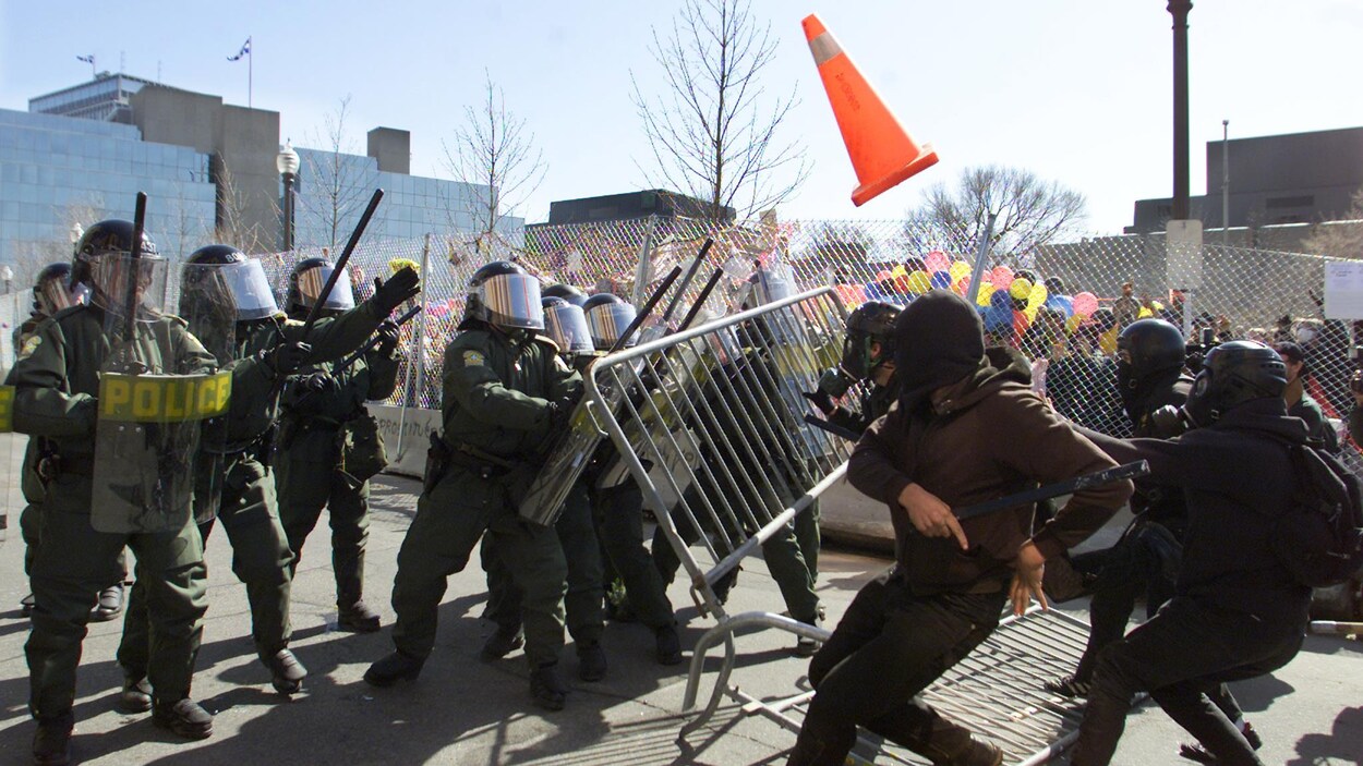 Des manifestants lancent un cône et poussent une clôture vers des policiers. Des manifestants lancent un cône et poussent une clôture vers des policiers.