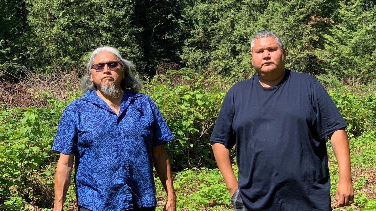 Les deux hommes affichent un air grave. Ils prennent la pose devant un bosquet.