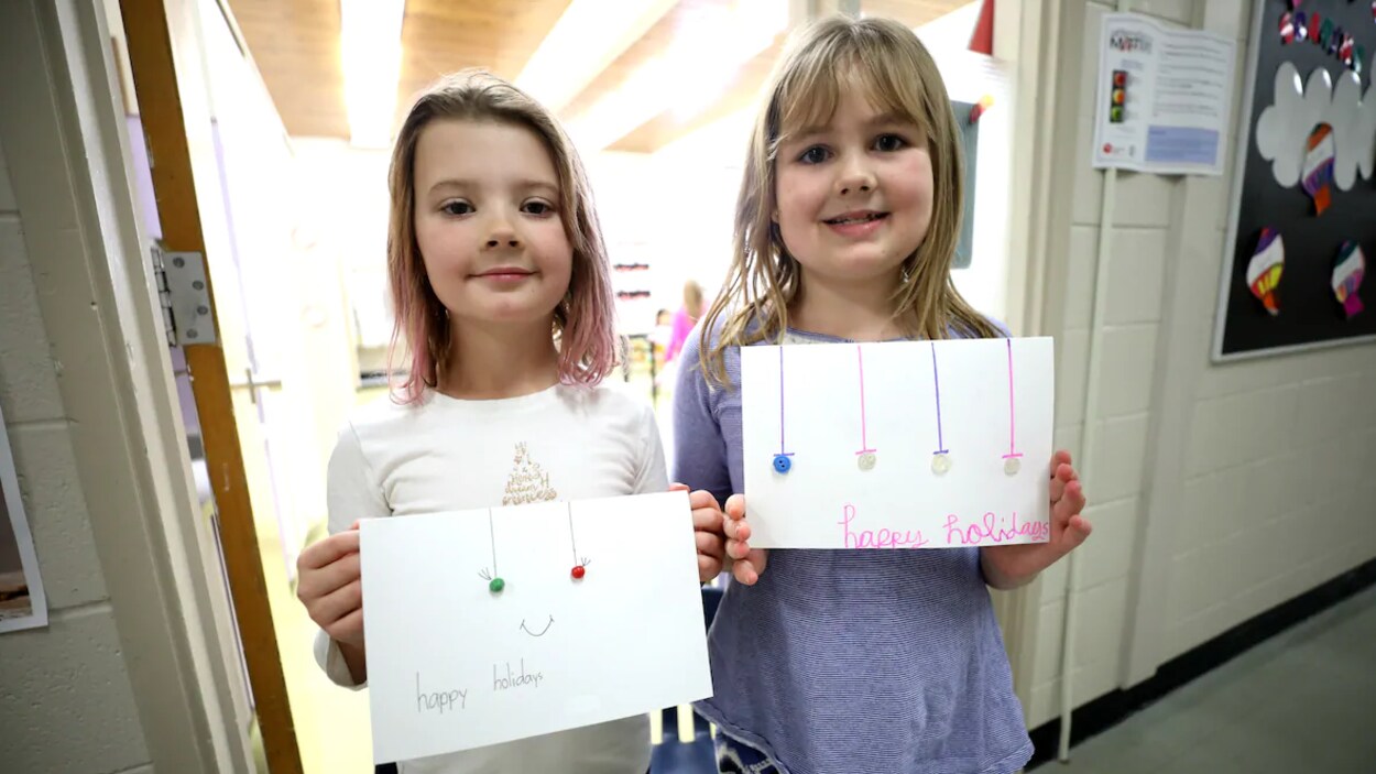 Deux petites filles dans le couloir de leur école tiennent dans leurs mains une carte souhaitant de joyeuses fêtes.