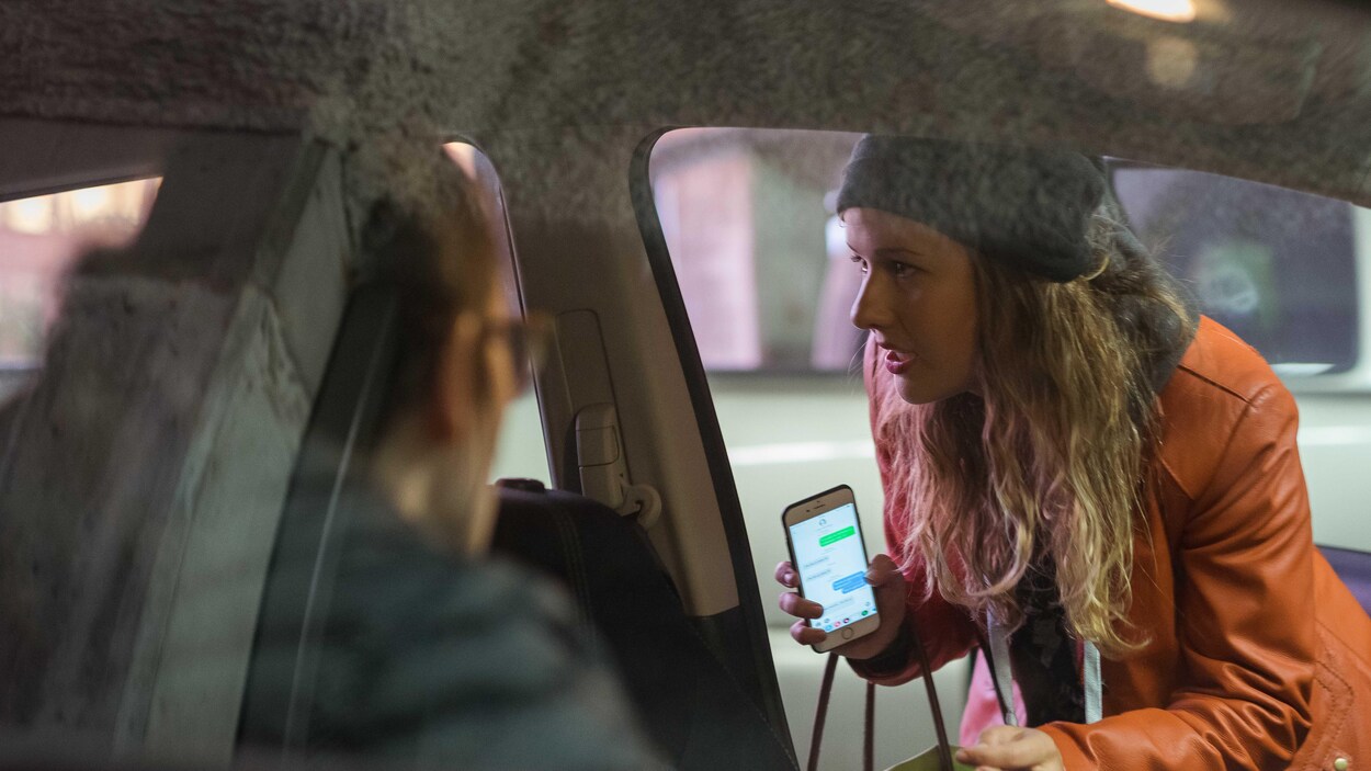 Une femme tient un téléphone cellulaire dans ses mains alors qu'elle rentre dans une voiture.