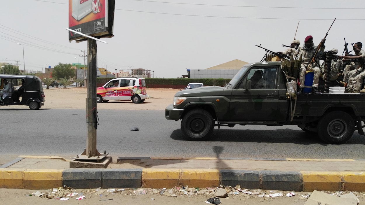 Des hommes sont assis à l'arrière d'une camionnette sur laquelle est montée une mitrailleuse. Ils tiennent des fusils d'assaut et sont vêtus en habit de camouflage.