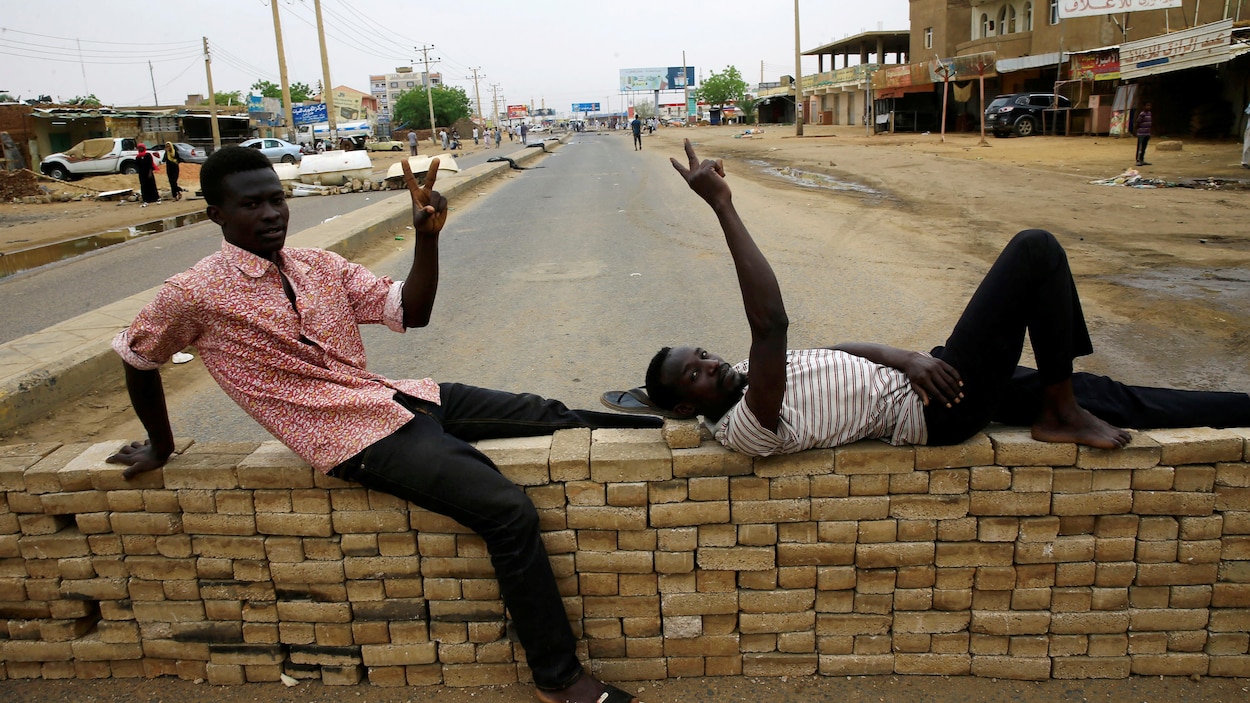 Deux manifestants font le V de la victoire sur une barricade de fortune en briques. La rue bloquée est pratiquement déserte.