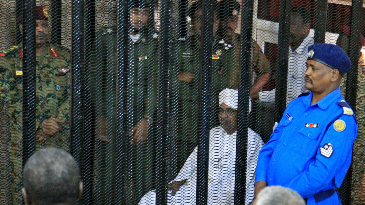 Le dirigeant militaire déchu du Soudan, Omar El-Béchir, est assis dans la cage des accusés dans un palais de justice.