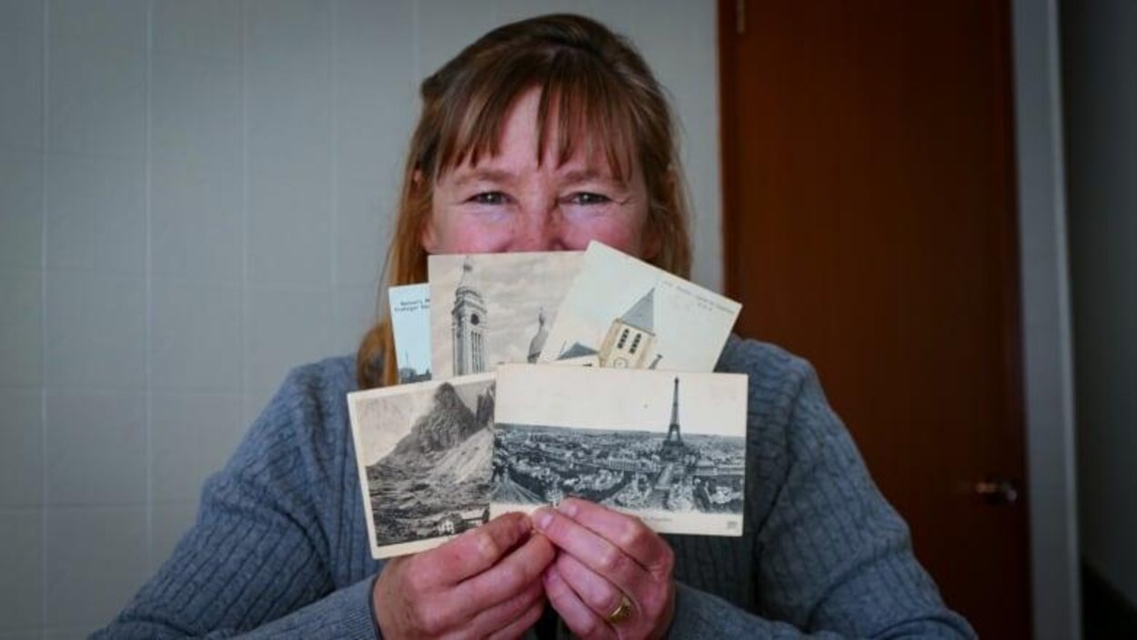 Une femme assise qui tient entre les mains, devant son visage, des cartes postales.
