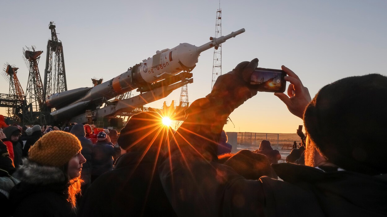 Des spectateurs regardent la fusée être installée sous le soleil levant.