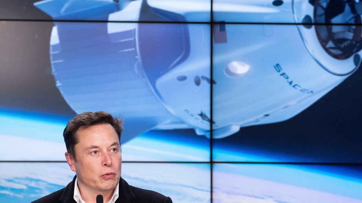 Elon Musk devant un écran montrant une capsule spatiale de SpaceX en orbite au-dessus de la Terre.