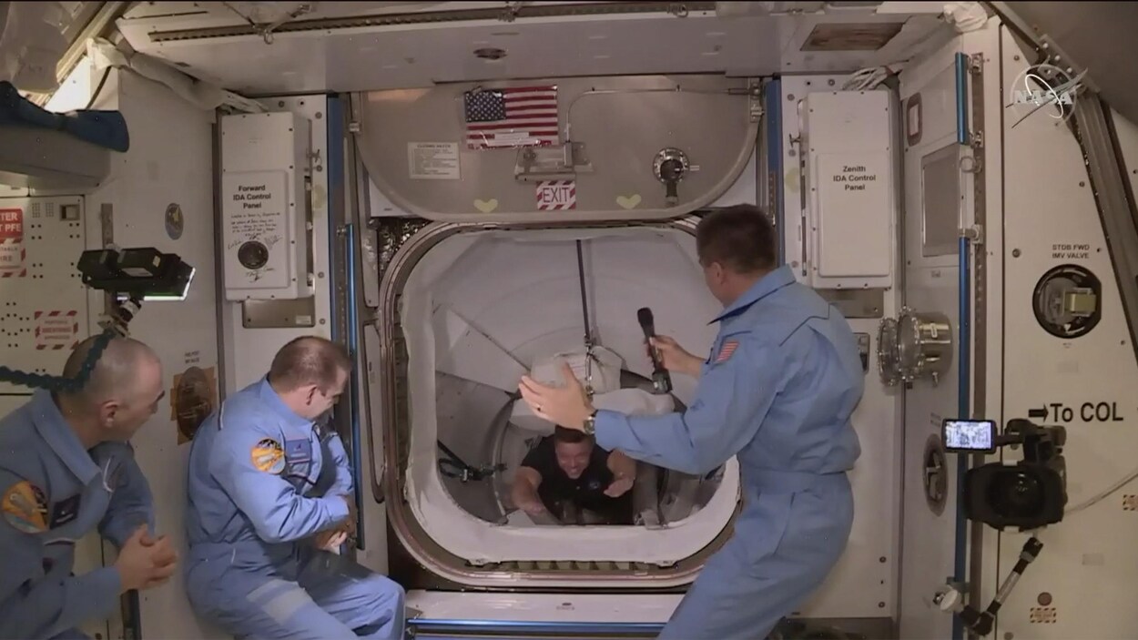 L'astronaute, en suspension, passe par un sas pour rejoindre les trois astronautes déjà sur place qui l'attendent.