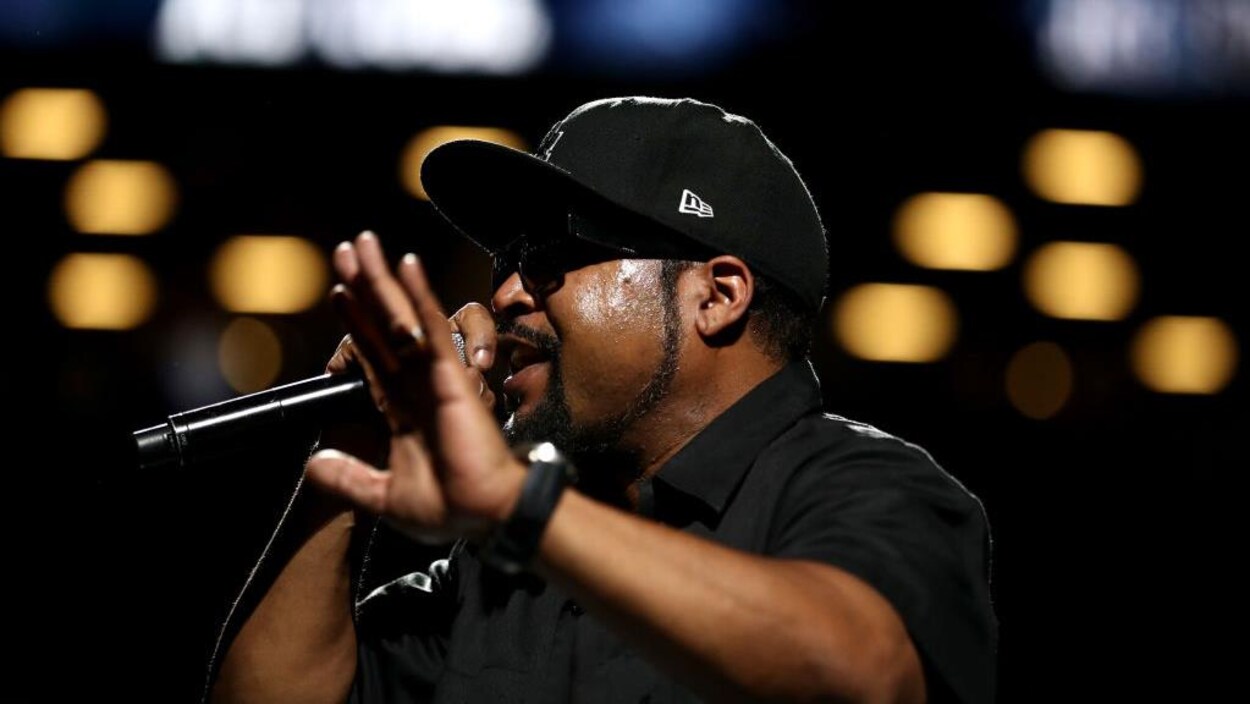 Ice Cube rappe sur scène, vêtu d'une chemise noire et arborant une casquette.
